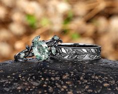 two wedding rings with green stones on top of each other, sitting on a rock