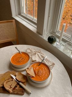 two bowls of carrot soup on a table with bread and crackers next to it