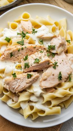 a white plate topped with pasta and chicken covered in cream sauce, garnished with parsley