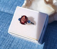 This is a big, bold Oregon Sunstone Ring.  This Oval sunstone is concave cut for brilliance, this type of cut draws more light into the stone so that it shines.  The stone is a nice bright Red.  The stone is 8 x 10 mm, 3.00 cts.  It is accented by 2 Blue, 3mm Montana Sapphires.  Are you looking to make a statement?  This ring will do it! #01 Round Orange Moonstone Ring, Orange Moonstone Ring, Oregon Sunstone Ring, Orange Gemstone-accented Ring Jewelry, Sunstone Ring, Montana Sapphires, Oregon Sunstone, Montana Sapphire, Jade Ring