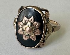 this ring has been very much loved and loved again, but still standing and maybe all the more beautiful for that love.  it's an homage to flowers and maybe was worn as a mourning ring.  there are at least two shades of 10k gold in there, and a black onyx that has some surface wear but no chips or cracks.  inner band is marked Esemco and has a worn gold mark.  Esemco started out in 1906, and went into 1972, I imagine this was one of their early ones.  has been sized. size:  measures a 6, may fit more like a 6.25 height of face:  5/8" width of inner band:  1mm weight:  2.8g Vintage Oval Flower Ring Hallmarked, Vintage Oval Hallmarked Flower Ring, Vintage Flower Engraved Ring For Anniversary, Antique Flower Jewelry For Anniversary, Heirloom Oval Flower Ring Hallmarked, Vintage 14k Gold Flower Ring, Vintage Yellow Gold Flower Ring, Vintage 14k Stamped Enamel Ring For Anniversary, Vintage 14k Gold Flower Ring For Anniversary