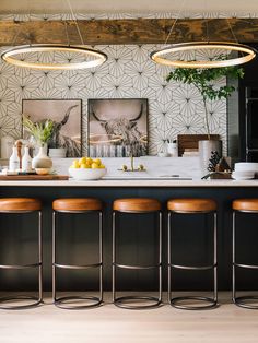 a kitchen with three stools and an island in front of the bar area, surrounded by potted plants