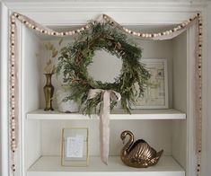 a white shelf with a wreath and other items on it, including a swan ornament