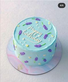 a blue birthday cake with purple flowers on the top and happy birthday written in frosting