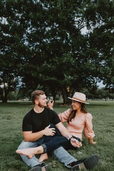 a man and woman sitting on the grass drinking wine