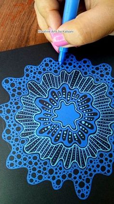 a hand holding a blue pen over a black notebook with an intricate design on it