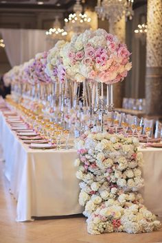 a table topped with lots of flowers next to tall vases filled with wine glasses