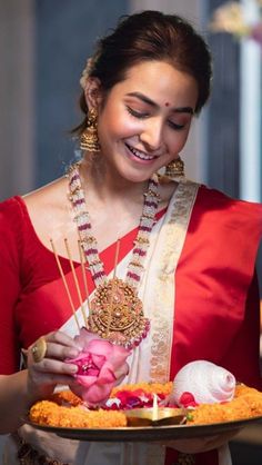 a woman in a red and white sari holding a tray with food on it