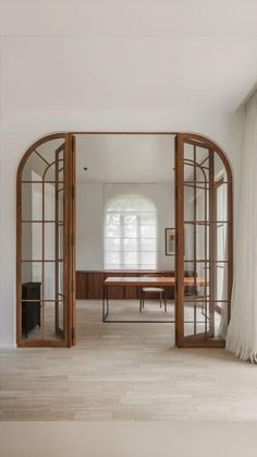 an open door leading to a dining room with wooden furniture and white drapes on the windows