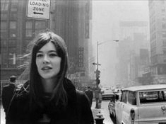 a woman standing in the middle of a city street next to tall buildings and traffic signs