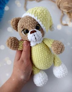 a hand holding a small teddy bear in yellow and white crochet with one eye open