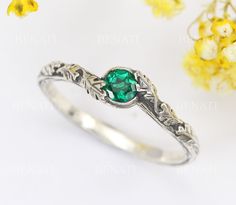 Exclusive to Benati. Emerald ring with a vintage and floral theme, will be a gorgeous engagement ring and make you/her instantly fall in love with.  With a incredible brilliance and beautiful green colour gem, you will enjoy this nature inspired ring everyday. Gem The emerald is a approx. 0.30 carat, approx. 4mm eco-friendly synthetic emerald.  The ring can also be crafted with a natural emerald gemstone. For a quote please contact us. The band The durable band has a unique wood carving texture Elegant Flower Ring As Promise Ring With May Birthstone, Vintage Emerald Rings For Wedding, Nature-inspired Round Flower Ring For Anniversary, Vintage Emerald Ring With Bezel Setting For Wedding, Handmade Vintage Emerald Ring For Anniversary, Elegant Green Flower Ring In Sterling Silver, Elegant Green Sterling Silver Flower Ring, Vintage Engraved Emerald Ring For Anniversary, Vintage Handmade Emerald Anniversary Ring