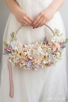 a woman wearing a white wedding dress holding a flowered basket in her hands,