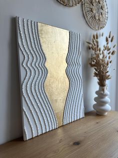 a white and gold art piece sitting on top of a wooden table next to a vase