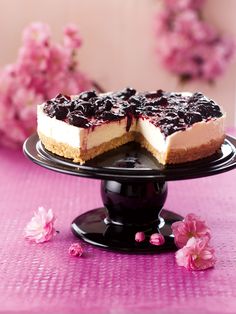 a cheesecake on a black cake stand with pink flowers in the backgroud