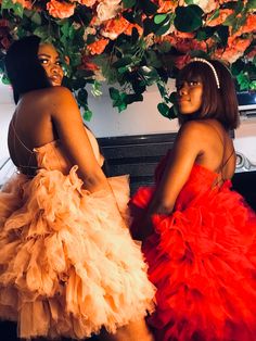 two women in dresses sitting next to each other on a couch with flowers behind them