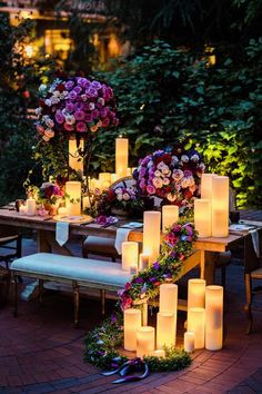 a table with candles and flowers on it in the middle of a garden at night