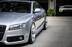 the front end of a silver car parked in a driveway next to another white car