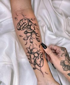 a person with a tattoo on their arm holding onto a flower and leaves braceleted to the wrist