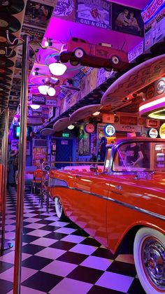 an orange car is parked in front of some surfboards on the wall and checkered floor