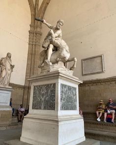 people sitting on the steps and looking at statues in a large room with high ceilings