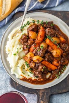 a plate with mashed potatoes, meat and gravy next to two glasses of wine