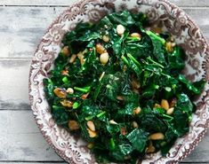 a bowl filled with greens and nuts on top of a wooden table