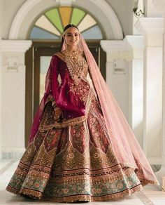 a woman in a red and gold wedding dress standing on a white floor with an archway behind her