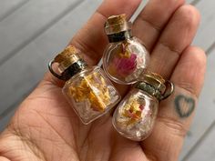 three tiny glass bottles with flowers inside in someone's hand, one is filled with water and the other is empty