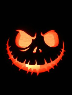 a carved jack o lantern in the dark with glowing eyes and fangs on it's face