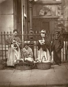 an old black and white photo of three people standing in front of a fence with baskets