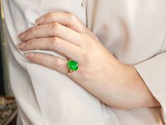 a woman's hand with a green ring on her left wrist, wearing a white shirt