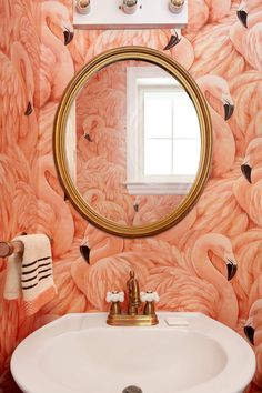 a bathroom with pink flamingos painted on the wall and a round mirror above it