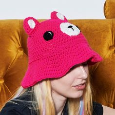 a woman wearing a pink crocheted hat with white eyes and ears on her head