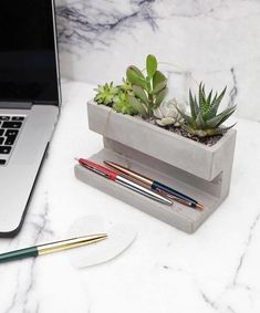 a laptop computer sitting on top of a desk next to a planter with succulents in it