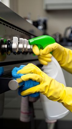 a person in yellow gloves is cleaning an oven with a green sprayer and sponge