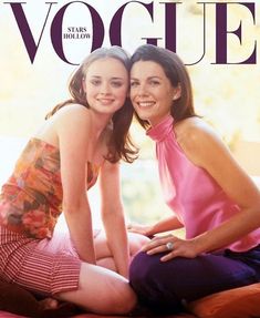 two women are sitting on the bed posing for a photo together, one is wearing a pink top and the other has a striped skirt