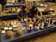 two women sitting at a table covered with pottery and other items in front of them