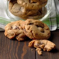 chocolate chip cookies sitting on top of a wooden table next to a glass jar filled with milk