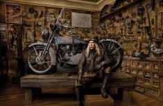 a man with long hair sitting on a bench next to a motorcycle in a room