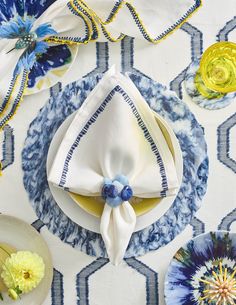 a blue and white table cloth with plates, napkins, and flowers on it