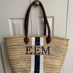 a straw bag hanging on the front door with initials and stripes painted on it's side