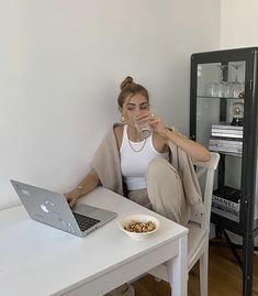 a woman sitting at a table with a laptop drinking water