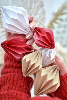 a person holding three origami pieces in their hands, one is red and the other is white