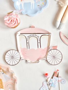 a pink and white horse drawn carriage with cupcakes on the table next to it