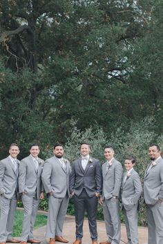 a group of men standing next to each other in front of some green trees and bushes