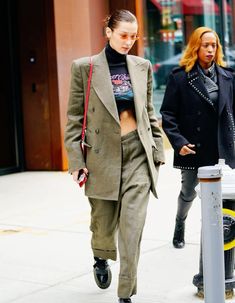 two women are walking down the street in front of a parking meter and one is wearing an oversize suit