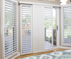 a living room with white shutters and a rug on the floor in front of it