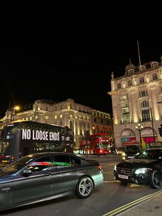 two cars parked in front of a double decker bus on a city street at night