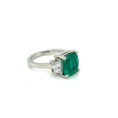 This Elegant Platinum three stone ring has a Natural Cushion Cut Colombian Emerald from the Top Muzo Mine with a GIA Certificate. The side stones are Natural Brilliant Cut Trapezoid Pair of Matching Diamonds. GIA#5202111099 3.34 Carat Cushion Modified 9.64x8.93x5.64 with moderate F2 clarity enchancement. 2 Matching Trapezoid Brilliant Cut Diamonds weigh 0.71 carats total weight and are graded G in color and SI1 to SI2 in clarity. Platinum weight is 5.14 DWT. Ring can be sized. UNBEATABLE PRICE!! Luxury Three Stone Gemstones For Anniversary, Timeless Three Stone Emerald Ring For Formal Occasions, Formal Green Three Stone Jewelry, Three Stone Diamond Gemstones For Anniversary, Formal Green Three-stone Jewelry, Three Stone Diamond Gemstones For Wedding, Formal Three-stone Green Jewelry, Formal Three-stone Emerald Jewelry, Luxury Three Stone Emerald Jewelry